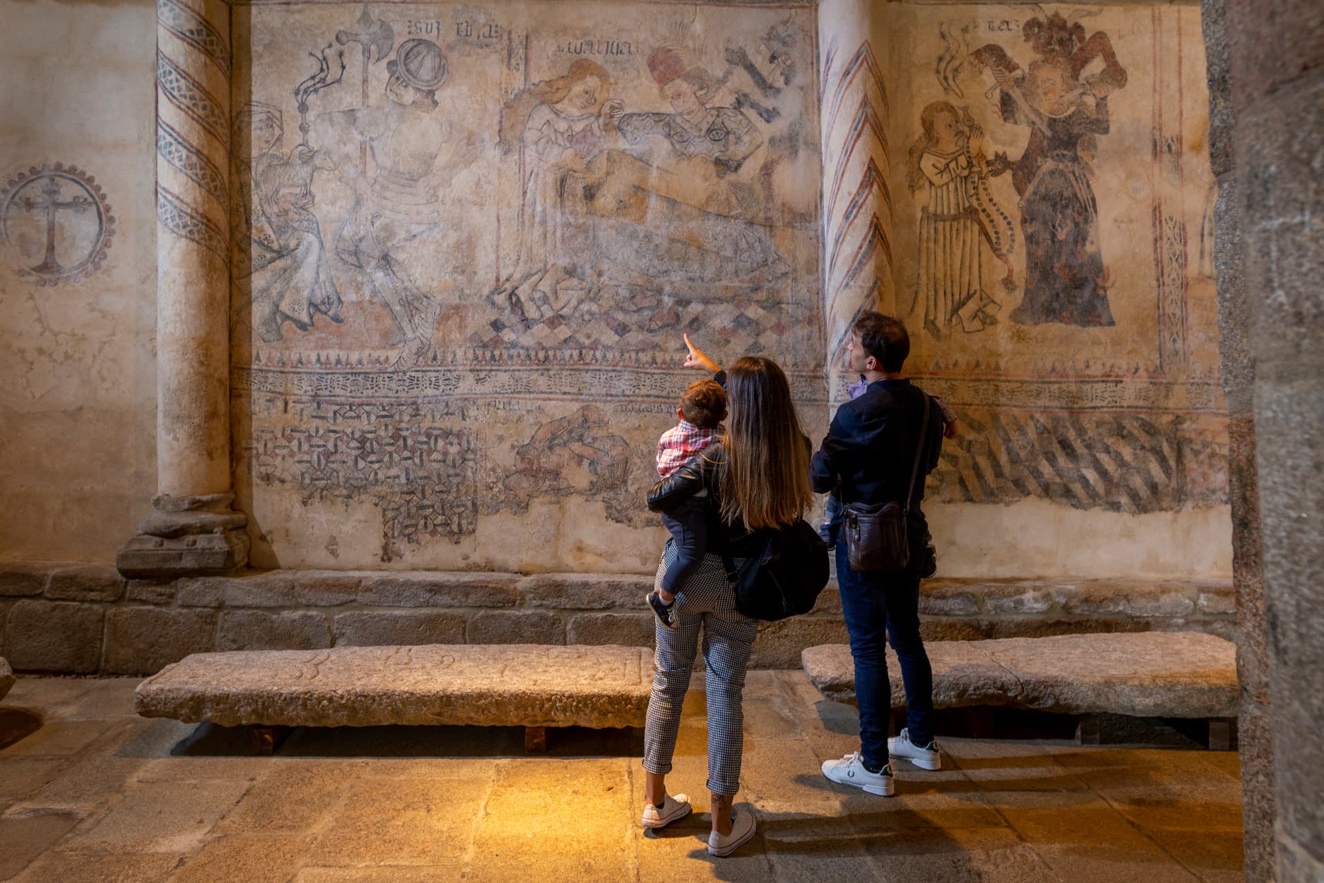 Familia observando las pinturas murales medievales de la iglesia de Moraime, en Muxía